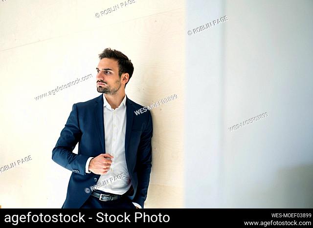 Young handsome businessman looking away while standing by wall