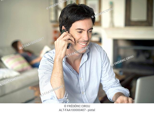Man talking on cell phone while using laptop computer