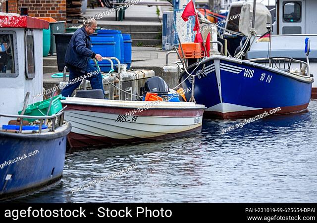 19 October 2023, Mecklenburg-Western Pomerania, Wismar: A man secures his boat at elevated water levels in the fishing port