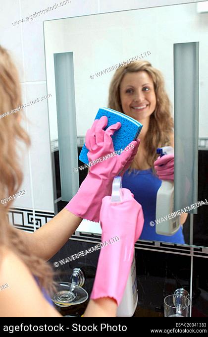 Smiling woman cleaning bathroom's mirror