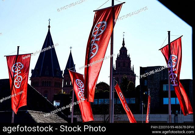 10 March 2022, Rhineland-Palatinate, Mainz: Flags with the Mainz city coat of arms are flying against the blue sky and the backdrop of the Mainz Cathedral