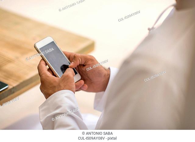 Close up of middle eastern man's hands using smartphone touchscreen at cafe, Dubai, United Arab Emirates