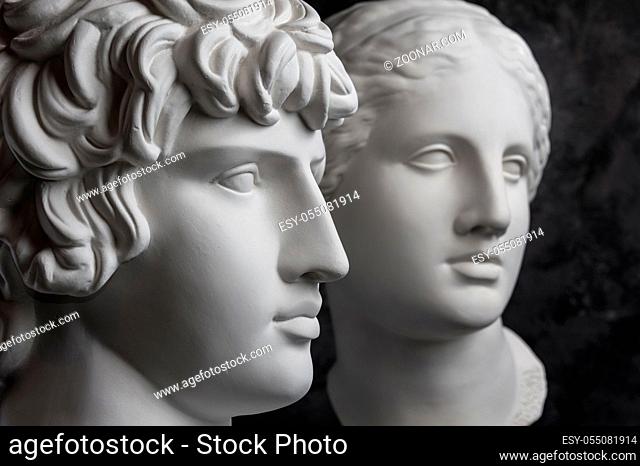 White gypsum copy of ancient statue of Antinous and Venus head for artists on a dark textured background. Plaster sculpture of statue face