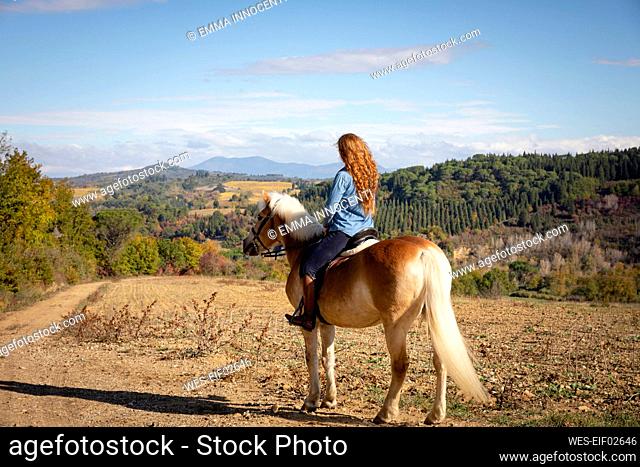 Woman sitting on horse at ranch on sunny day