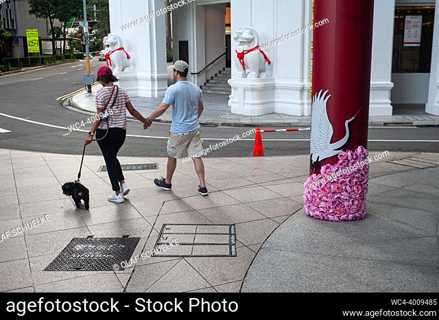 Singapore, Republic of Singapore, Asia - A couple walks on a footpath in the downtown district with their dog on the leash