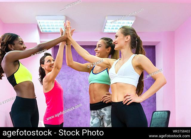 Happy fit women putting hands together as a gesture of determination and friendship before group workout class in a modern fitness club for ladies only