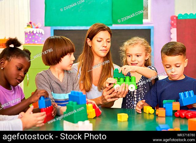 Gruppe Kinder spielt im Kindergarten mit Erzieherin mit Bausteinen am Tisch