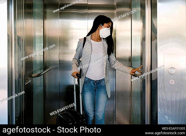 Woman wearing protective face mask pressing elevator button at station