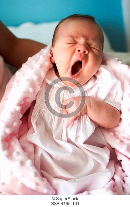 Tired baby yawning in mother's arms