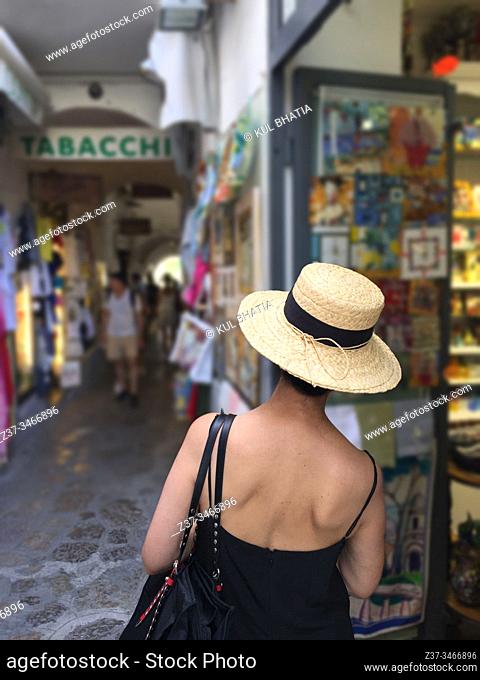 A woman in a straw hat and cool black dress walks in a trendy shopping street in summer, Ravello, the Amalfi Coast, Italy