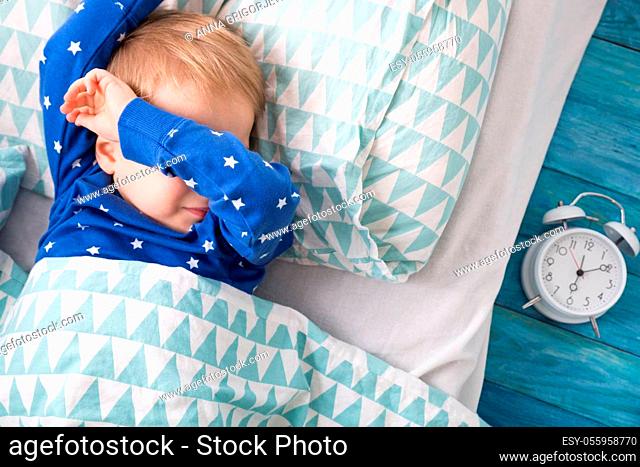 Three years old child crying in bed. Boy hiding and closing eyes with hands