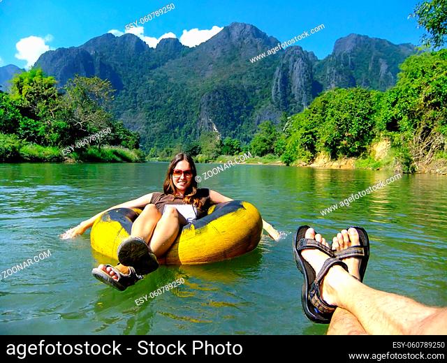 Couple going down Nam Song River in a tube surrounded by karst scenery in Vang Vieng, Laos. Tubing is a popular tourist activity in Vang Vieng