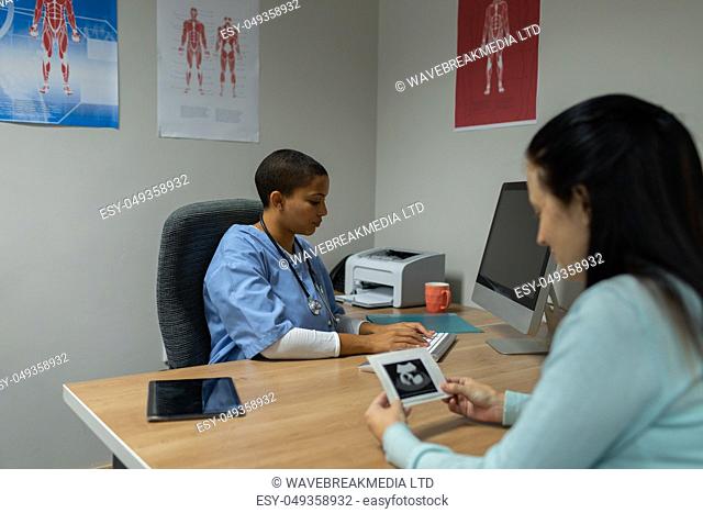 Front view of mixed-race female doctor working on computer while woman looking at ultrasound scan at desk in hospital