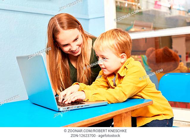 Junge und Lehrerin am Laptop Computer beim Lernen online im Kindergarten haben Spaß