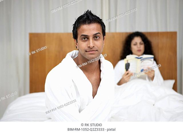 Middle Eastern man in bathrobe with woman reading in bed