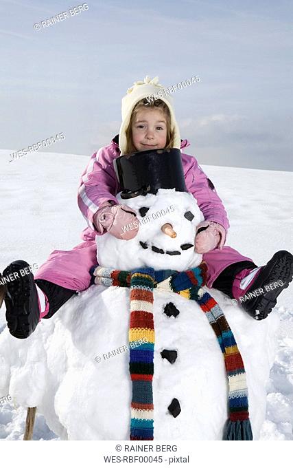 Germany, Bavaria, Munich, Girl 4-5 sitting on snowman, portrait