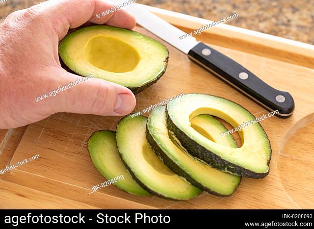 Male hand prepares fresh cut avocado on wooden cutting board
