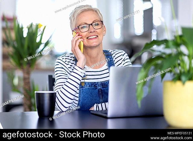 Mature businesswoman smiling while talking on smart phone at home office