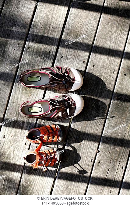 A pair of adult, and a pair of child's, water shoes, laying out on a porch in the summer sun to dry