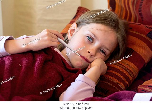Little girl lying on couch with digital thermometer