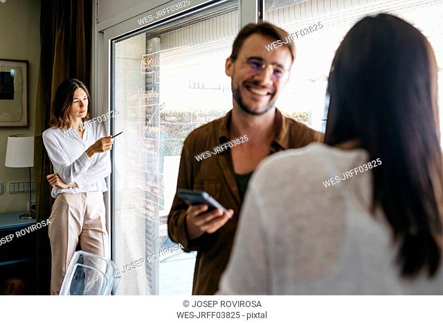 Woman writing on glass pane with coworkers in foreground