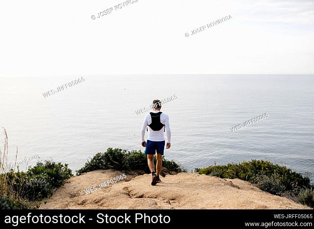 Man walking at cliff near sea against clear sky