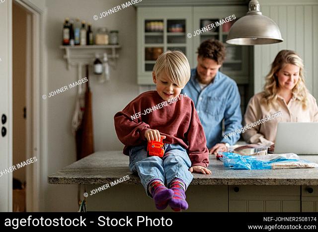Boy playing in kitchen, parents in background
