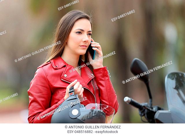 Portrait of a serious biker waiting during a phone call to insurance on a motorbike on the street