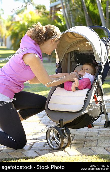 Young mother kneeling down checking on baby in stroller
