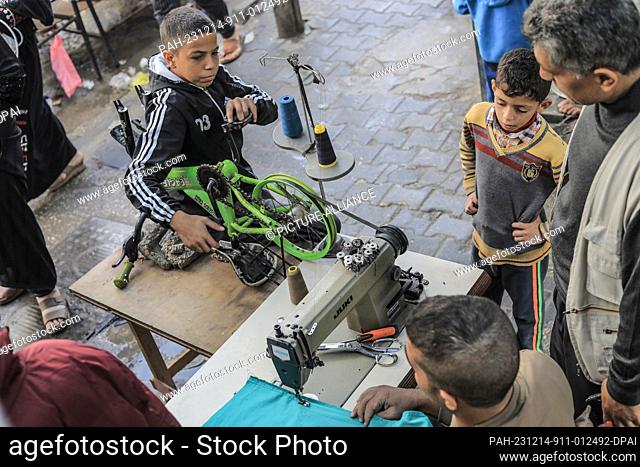 14 December 2023, Palestinian Territories, Rafah: Palestinian tailor Muhammad Qishta works in his workshop, ingeniously adapting to a power outage by rigging a...