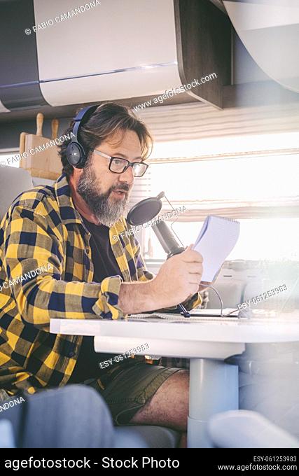 Modern adult man working with laptop and microphone inside a camper van in digital nomad job lifestyle. Technology and travel
