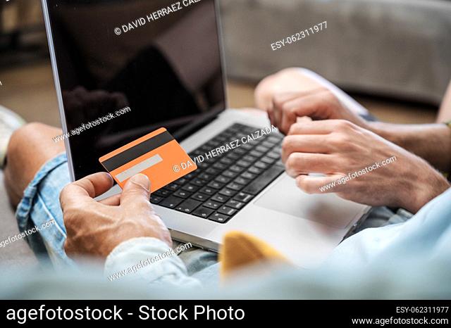 Close up of an unrecognizable gay couple using laptop computer while sitting on a couch at home, shopping online with a credit card
