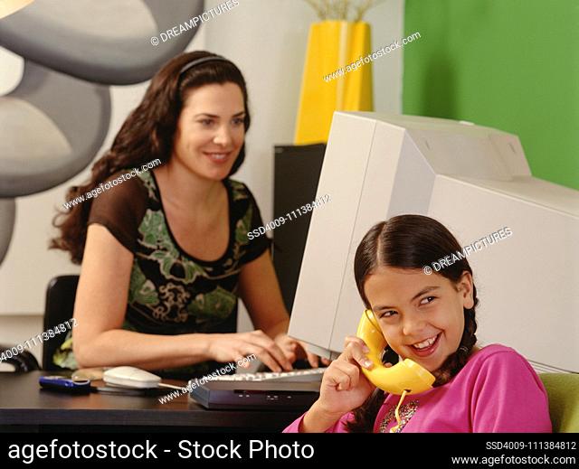 Daughter talking on telephone while mother works in background