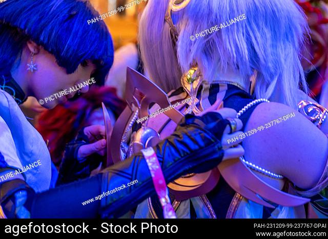 09 December 2023, Bavaria, Coburg: A young woman adjusts a detail on her friend's manga-style costume for a cosplay competition