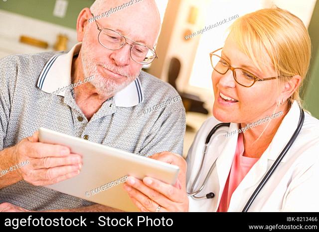 Female doctor or nurse showing senior man touch pad computer at home