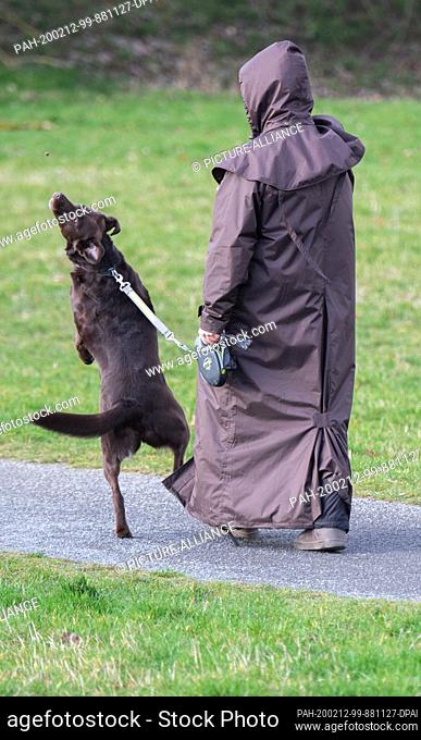 12 February 2020, Lower Saxony, Hanover: A woman in a brown rain cape throws a treat for her dog, who jumps after it. Photo: Julian Stratenschulte/dpa