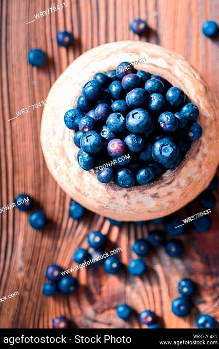 Freshly gathered blueberries put into old ceramic bowl. Some fruits freely scattered on old wooden table. Shot from above