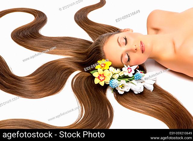 beautiful young woman with long hair lying on white floor. flowers. beauty studio shot. copyspace