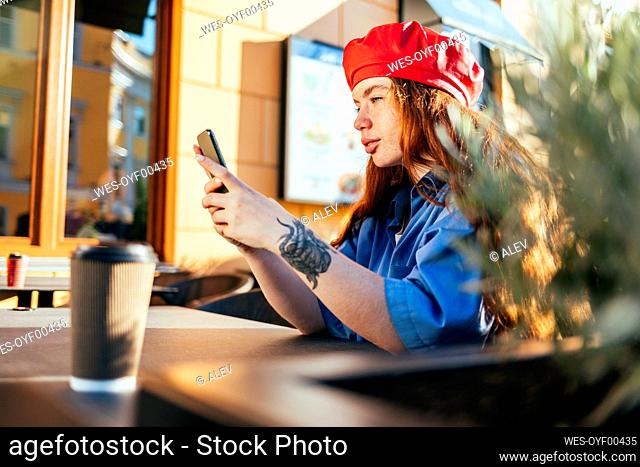 Young woman in beret hat using smart phone at sidewalk cafe