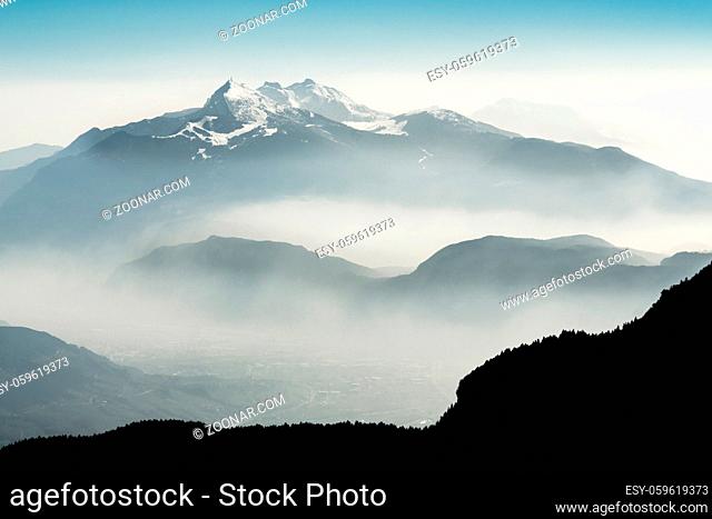 Beautiful view snow covered mountain ranges silhouettes and fog filled valleys with bright back light. South Tyrol, Itay, Alps
