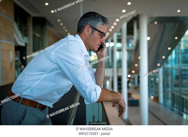 Businessman leaning on the railings while talking on the phone in office