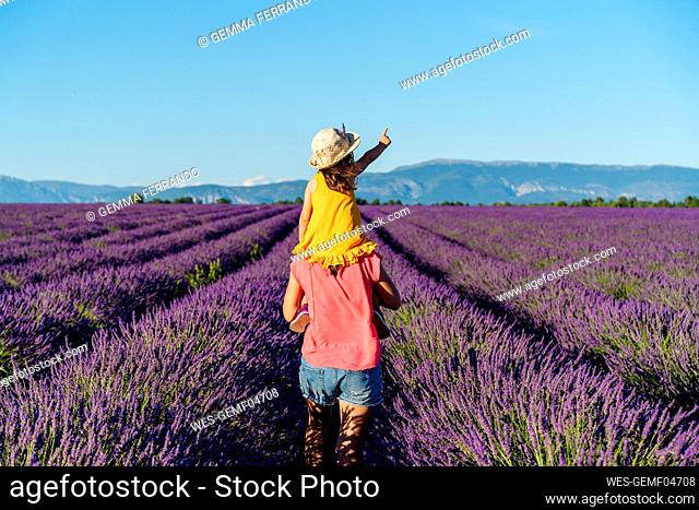 Mother piggybacking little daughter in vast summer lavender field