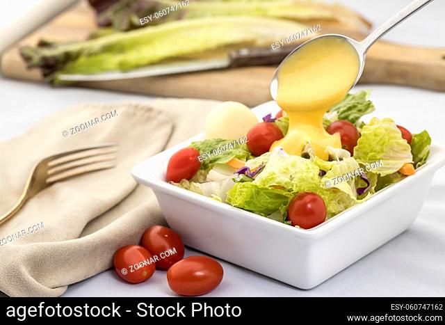 A studio image of a salad topped with cherry tomatoes and dressing being poured on it