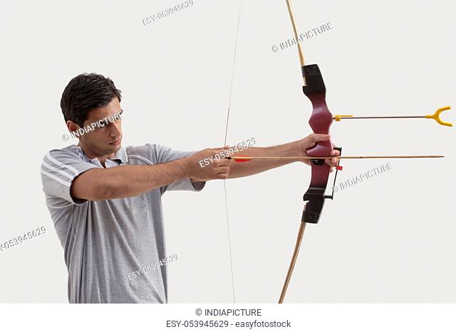 Male archer aiming bow and arrow against gray background