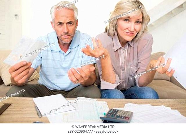 Tensed mature couple with bills and calculator at home
