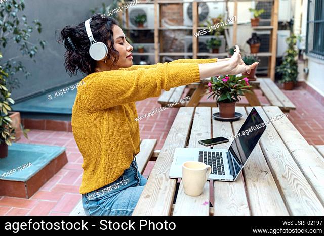 Businesswoman with eyes closed stretching arms sitting at cafe