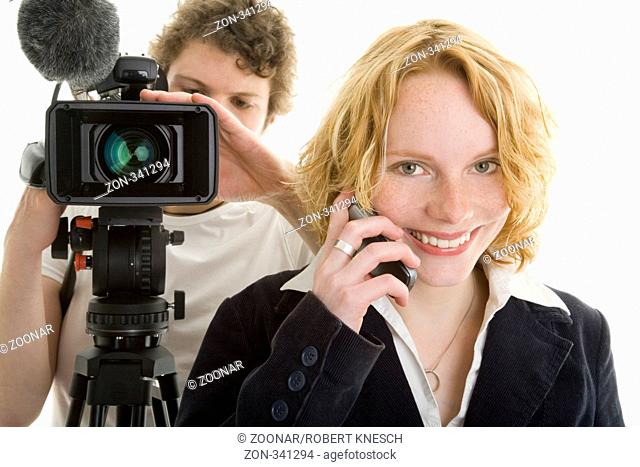 Fernsehjournalistin telefoniert mit ihrem Handy, während ihr Kameramann die Kamera einstellt