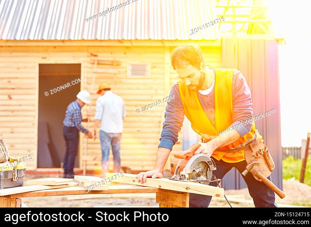 Handwerker mit Handkreissäge beim Hausbau vor einem Haus auf der Baustelle