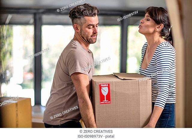 Couple in unfurnished home, carrying box of fragile belongings