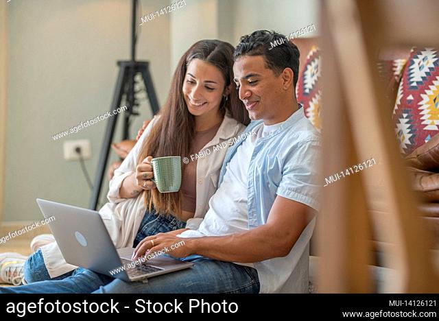 young boy and girl together at home enjoying laptop computer sitting on the floor smiling and laughing - new life married people in love and relationship have...